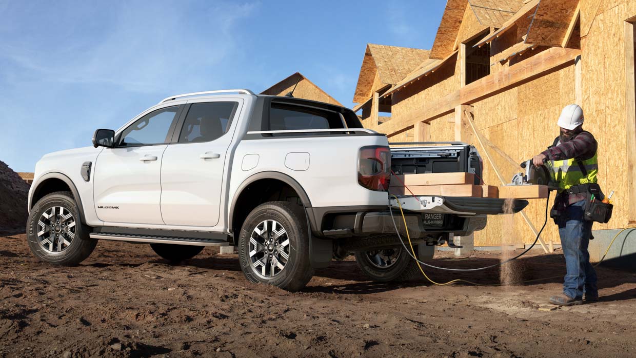 A Ford Ranger Wildtrak inch-in hybrid ute offering AC energy for instruments on an city worksite with a tradesman in physique